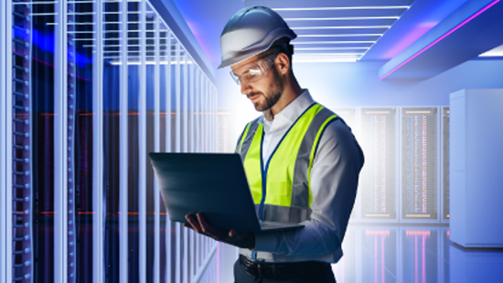 employee with PPE on looking at laptop in data center